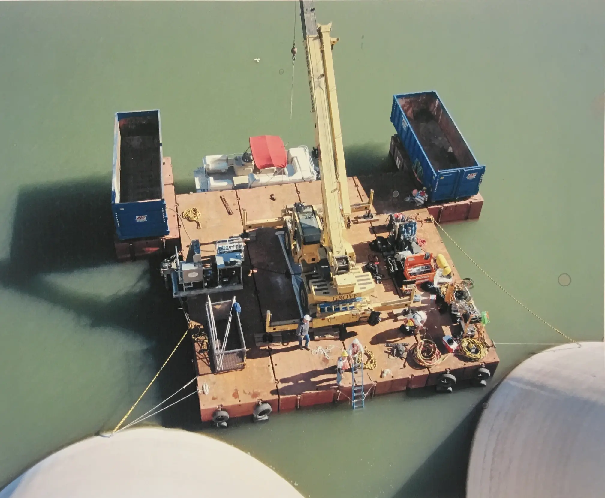 A fleet of equipment, including a rough terrain crane on barges, preparing for dam work, showcasing adaptability.