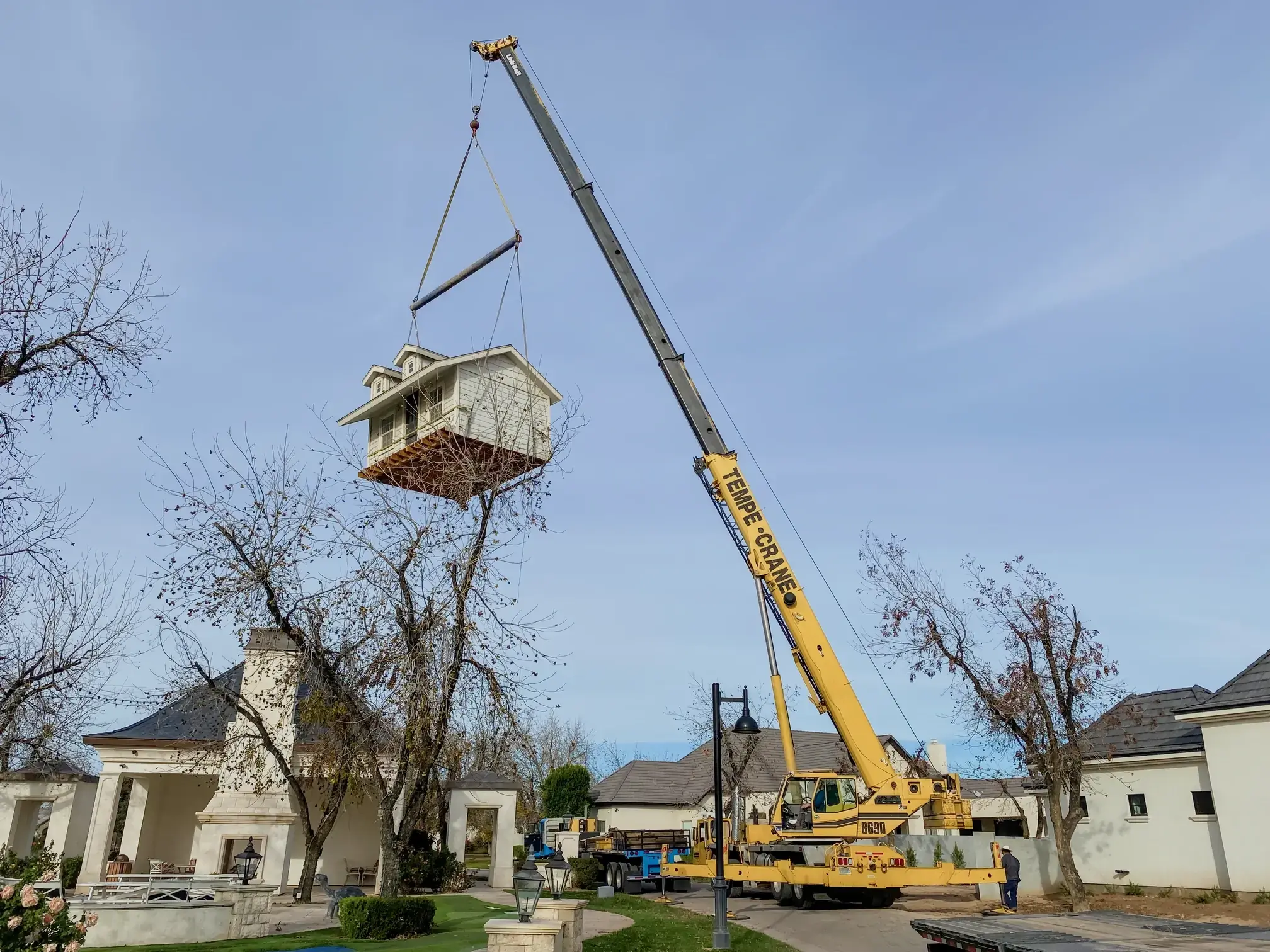A crane hoists a large shed over a home and into its new position, illustrating our specialized lifting capabilities.